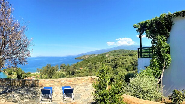 Une terrasse avec deux fauteuils bleus confortables, offrant une vue panoramique sur la mer et les collines.