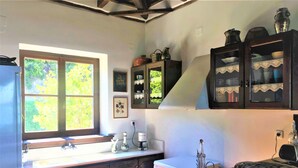 Une cuisine avec des meubles en bois, une fenêtre donnant sur un espace verdoyant, une machine à café et un vase posé sur le plan de travail.