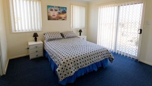 A bedroom with a bed, two bedside tables, a painting, and a large window with blinds. - 1/6 Convent Lane (Yamba)