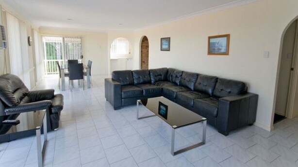 A modern living room with a sectional sofa, a coffee table, and a dining area with chairs. - 1/6 Convent Lane (Yamba)