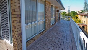 A balcony with a brick exterior, large windows, and a view of surrounding buildings and trees. - 1/6 Convent Lane (Yamba)