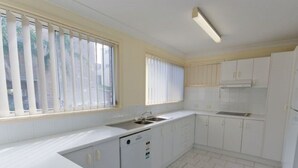 A kitchen with white cabinets, a sink, and a window with blinds. - 1/6 Convent Lane (Yamba)