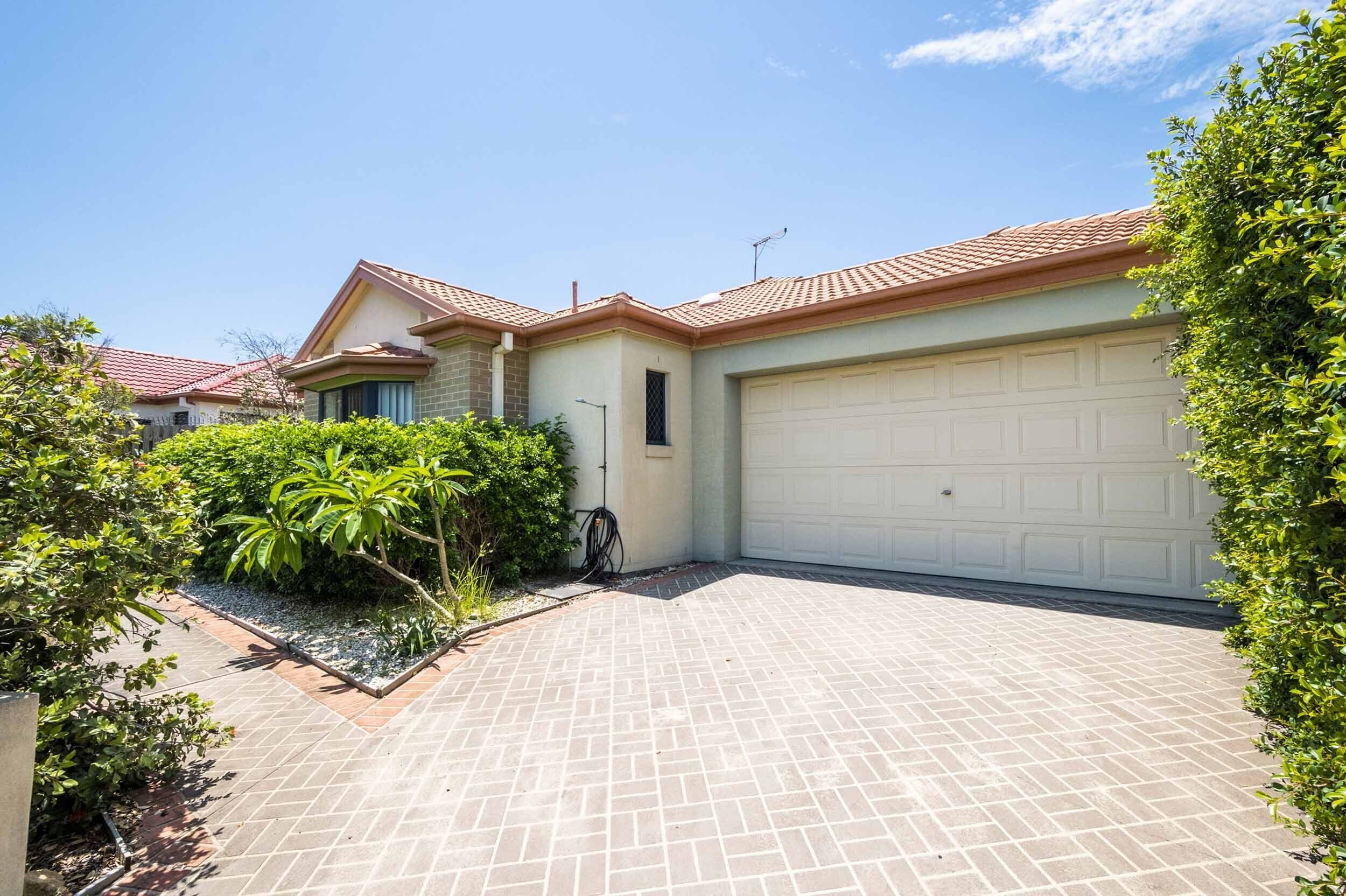 A residential house with a garage, paved driveway, and surrounding greenery.