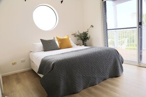 A bedroom with a bed, a round mirror, a potted plant, and a balcony with a railing. - Beaches 1 - 1/7 Convent (Yamba)