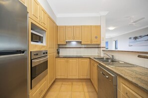 A modern kitchen with wooden cabinets, stainless steel appliances, and a granite countertop. - Breakers 2/12 (Yamba)