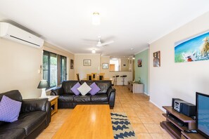A modern living room with a leather sofa, a wooden coffee table, and a TV stand with electronic devices. - Breather 2/44 Beachside Way (Yamba)