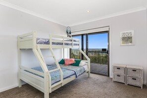 A bunk bed room with a balcony view, carpeted floor, and a small white side table.