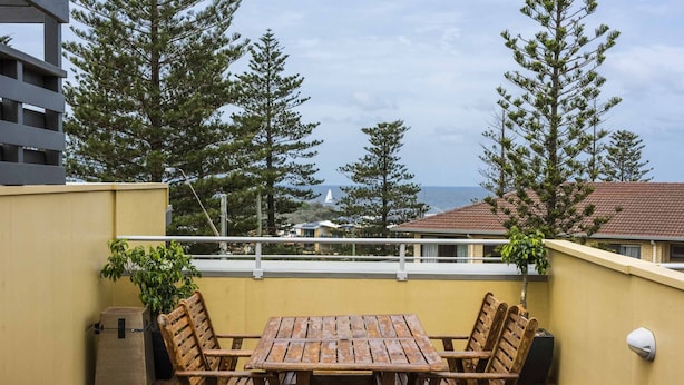Um deck de madeira com mesa e cadeiras, com vista para uma área costeira com árvores e edifícios.