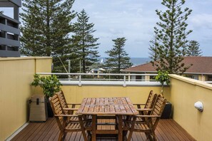 Um deck de madeira com mesa e cadeiras, com vista para uma área costeira com árvores e edifícios.