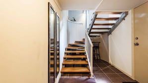 Escada com degraus de madeira e corrimãos de metal, levando a um quarto com porta e janela.