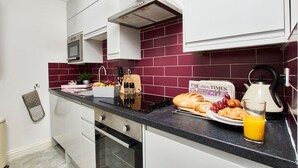 A modern kitchen with white cabinets, a black countertop, and a red-tiled backsplash. - Stylish Apt Near EMA; Gym & Pool Access, Fast WiFi (Castle Donington)