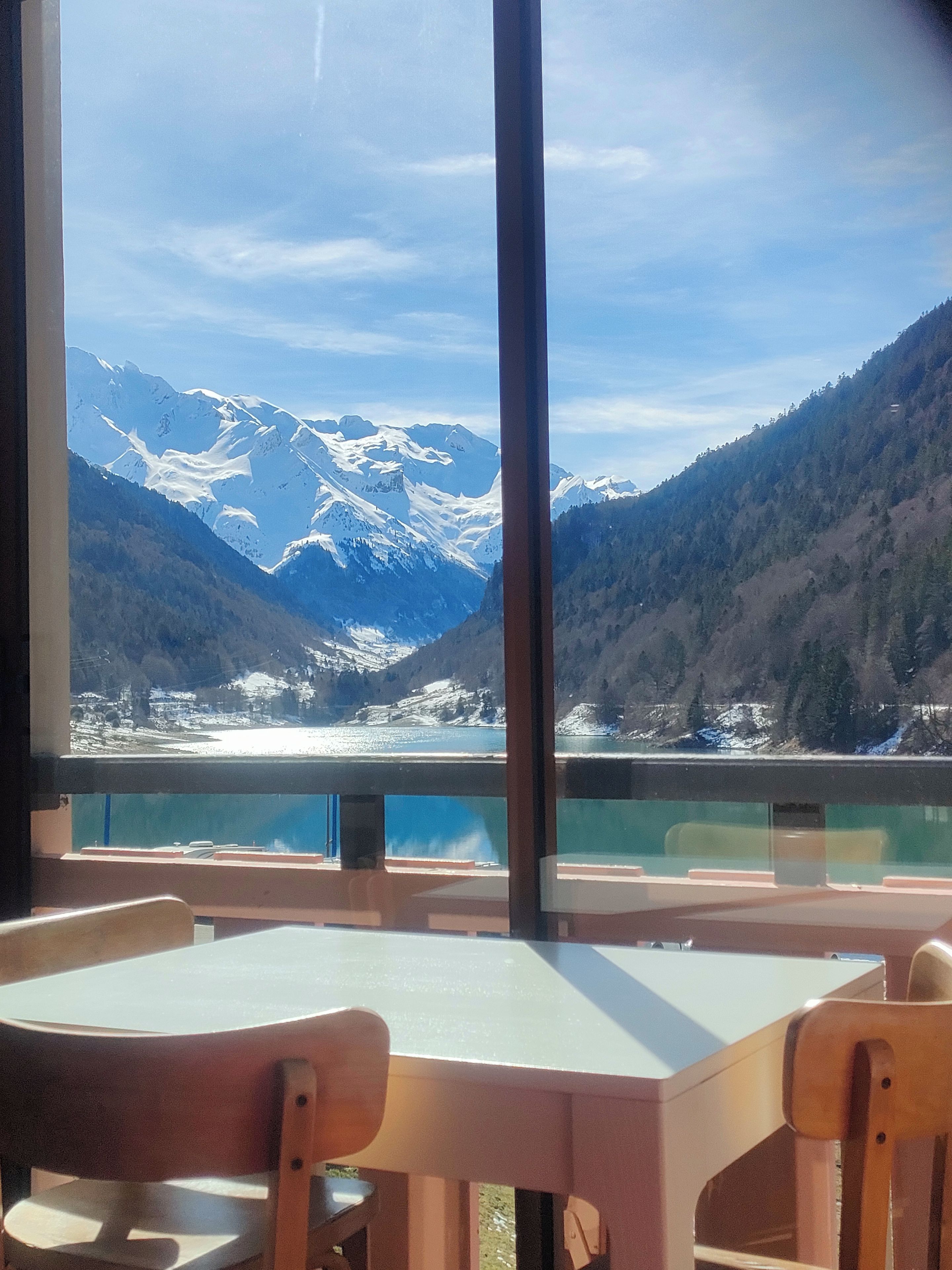 A dining area with a table and chairs, overlooking a mountainous landscape with a lake.