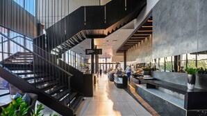 A modern hotel lobby with a central staircase, a reception desk, and a view of the outdoors. - The Capital Mbombela (Mbombela)