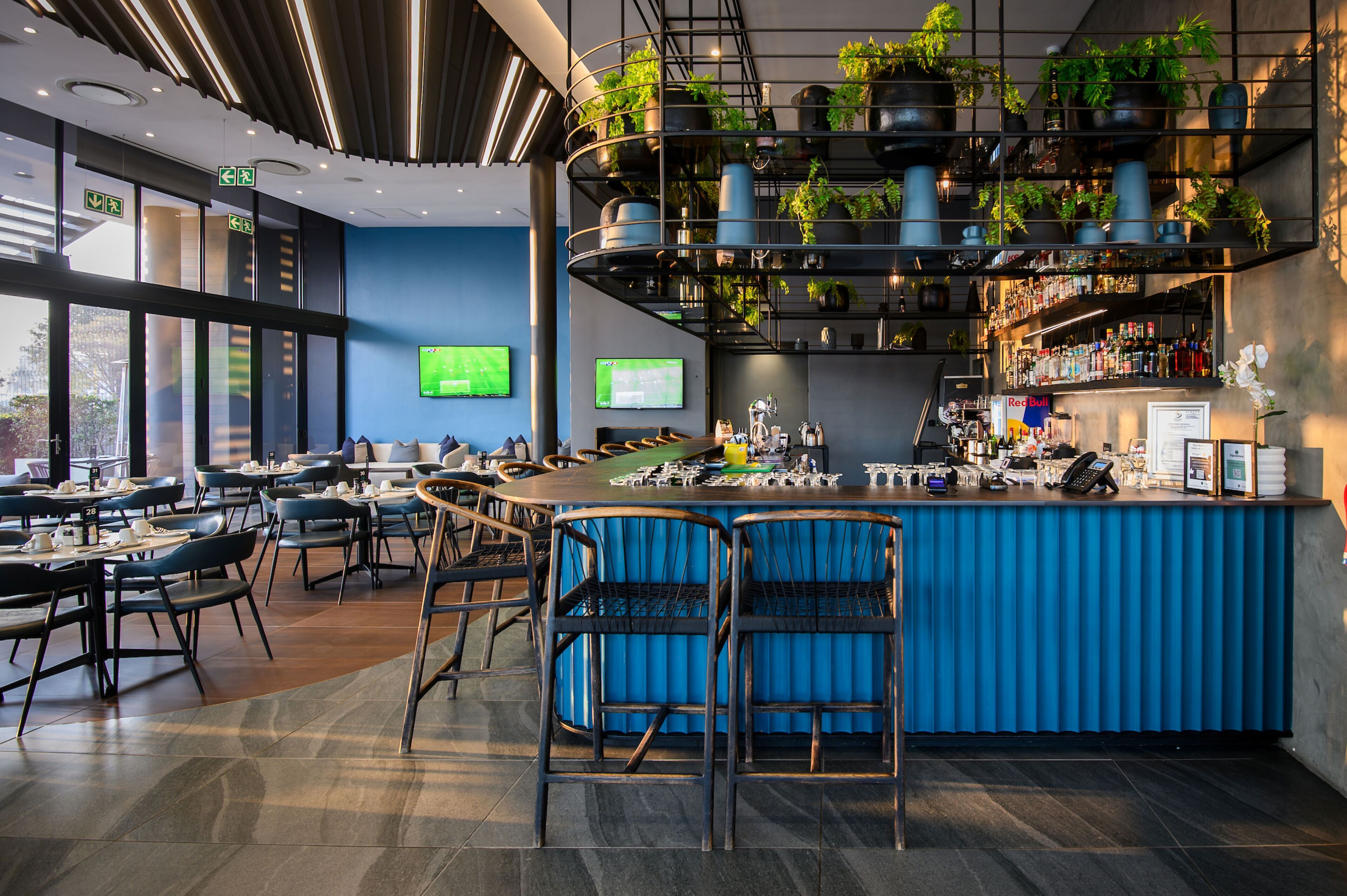 A modern bar area with a blue bar counter, seating, and a variety of plants.