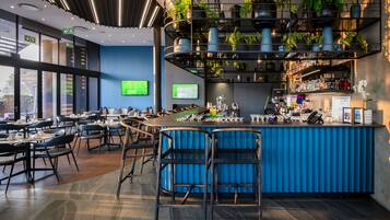 A modern bar area with a blue bar counter, seating, and a variety of plants.