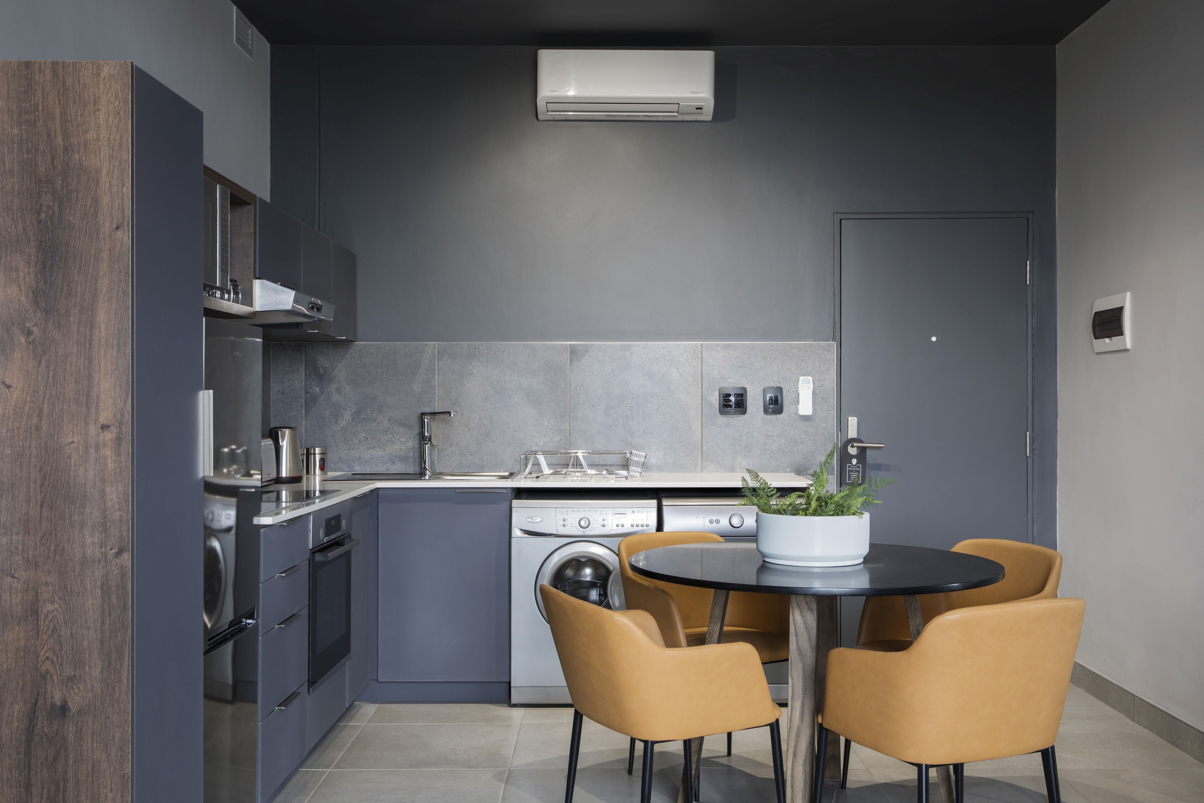 A modern kitchen with grey cabinets, a built-in oven, and a dining area with a round table and four chairs.