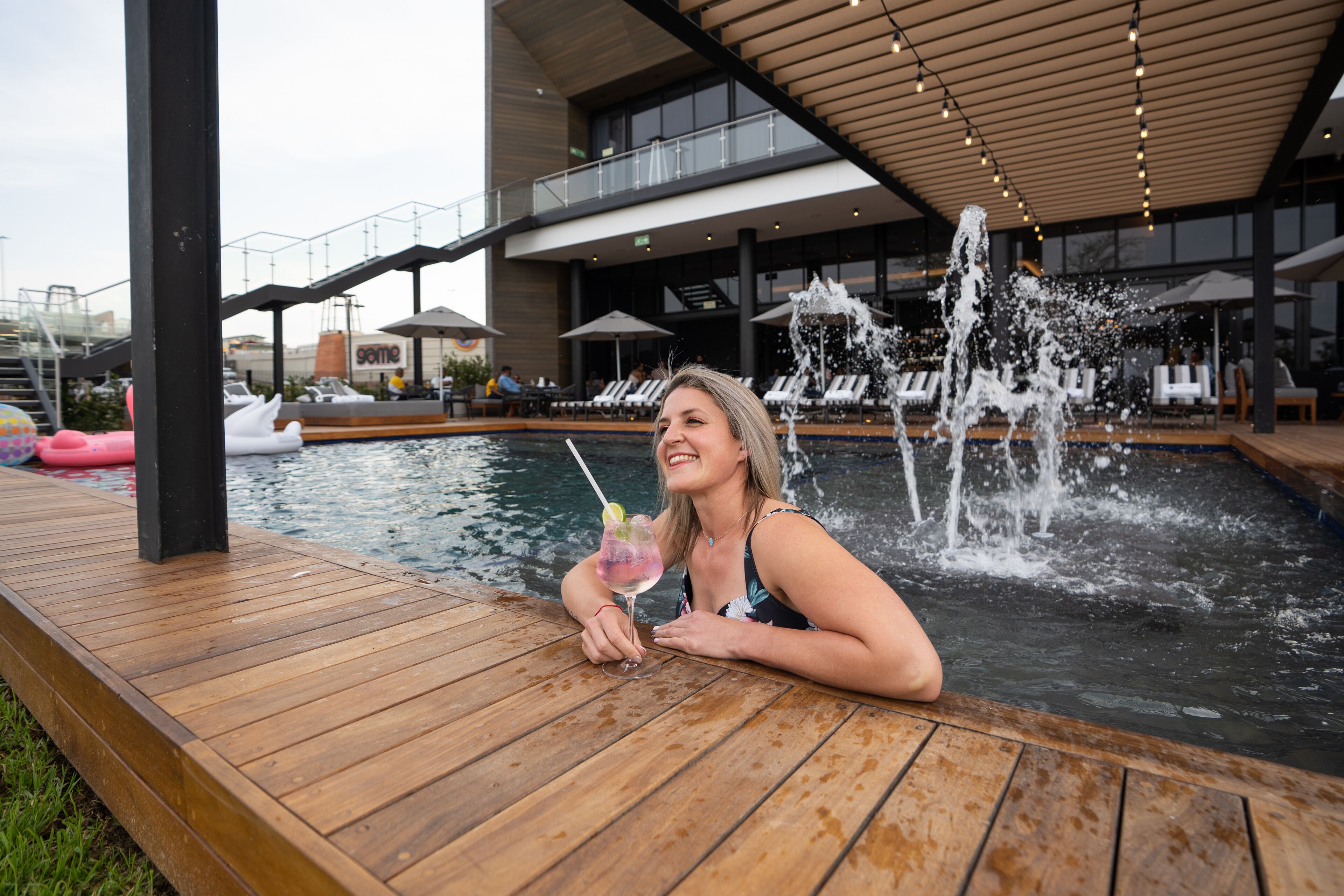 Ein Poolbereich mit Holzterrasse, Liegestühlen und einer Fontäne.
