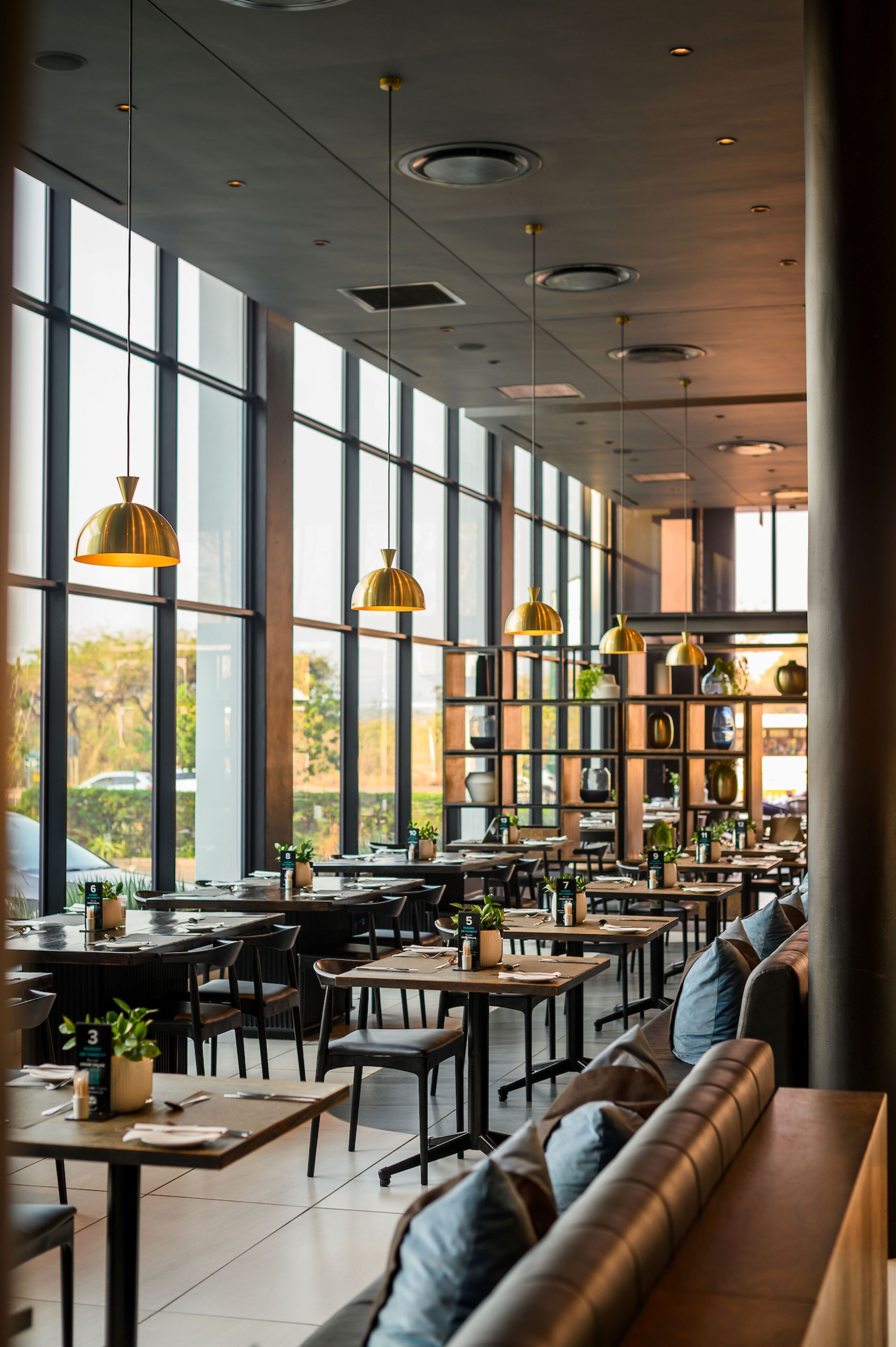 A spacious restaurant with high ceilings, large windows, and modern pendant lighting. Tables and seating are arranged for dining.