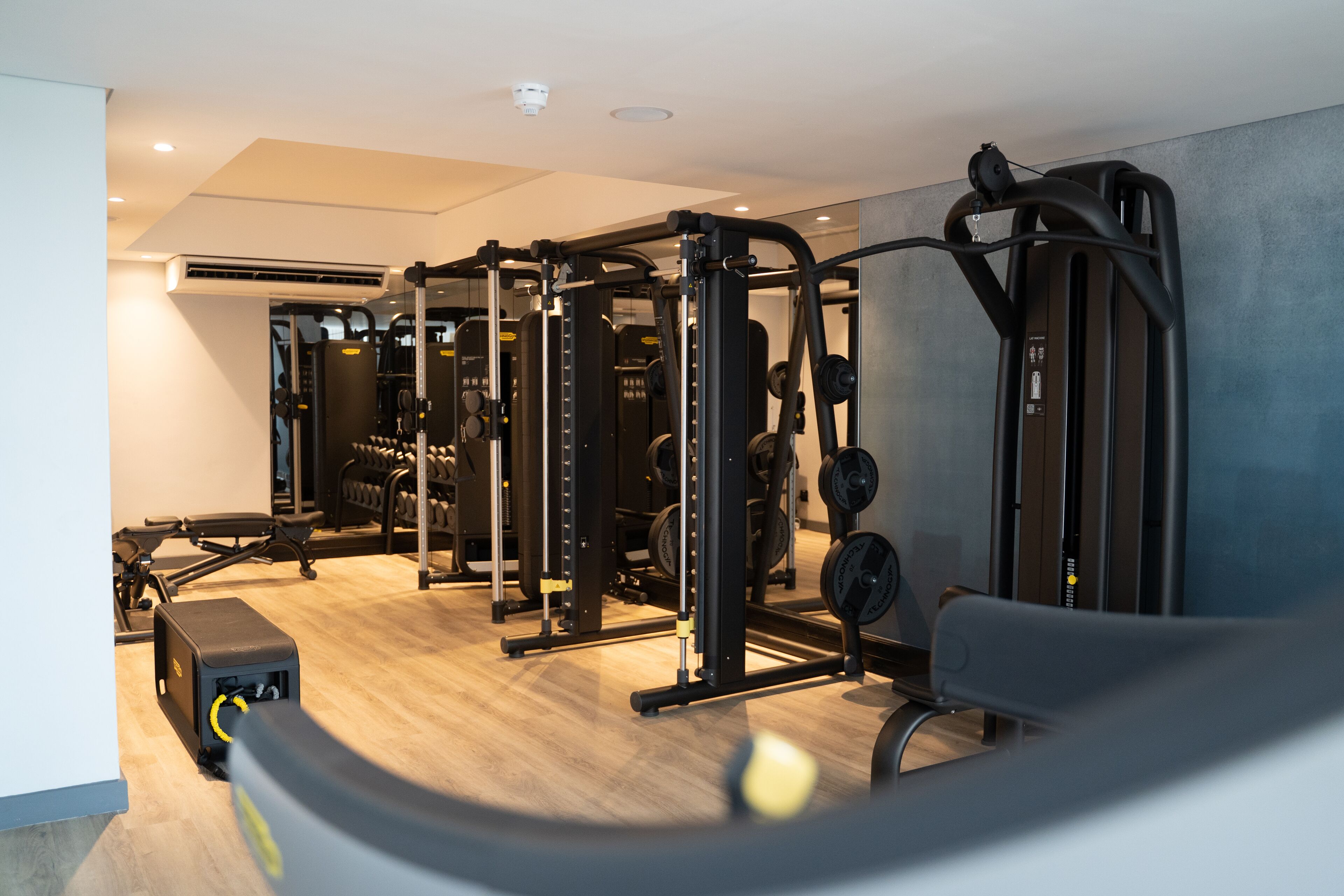 Un gimnasio con diversos equipos de ejercicio, incluyendo máquinas de pesas y pesas libres, además de una banca.