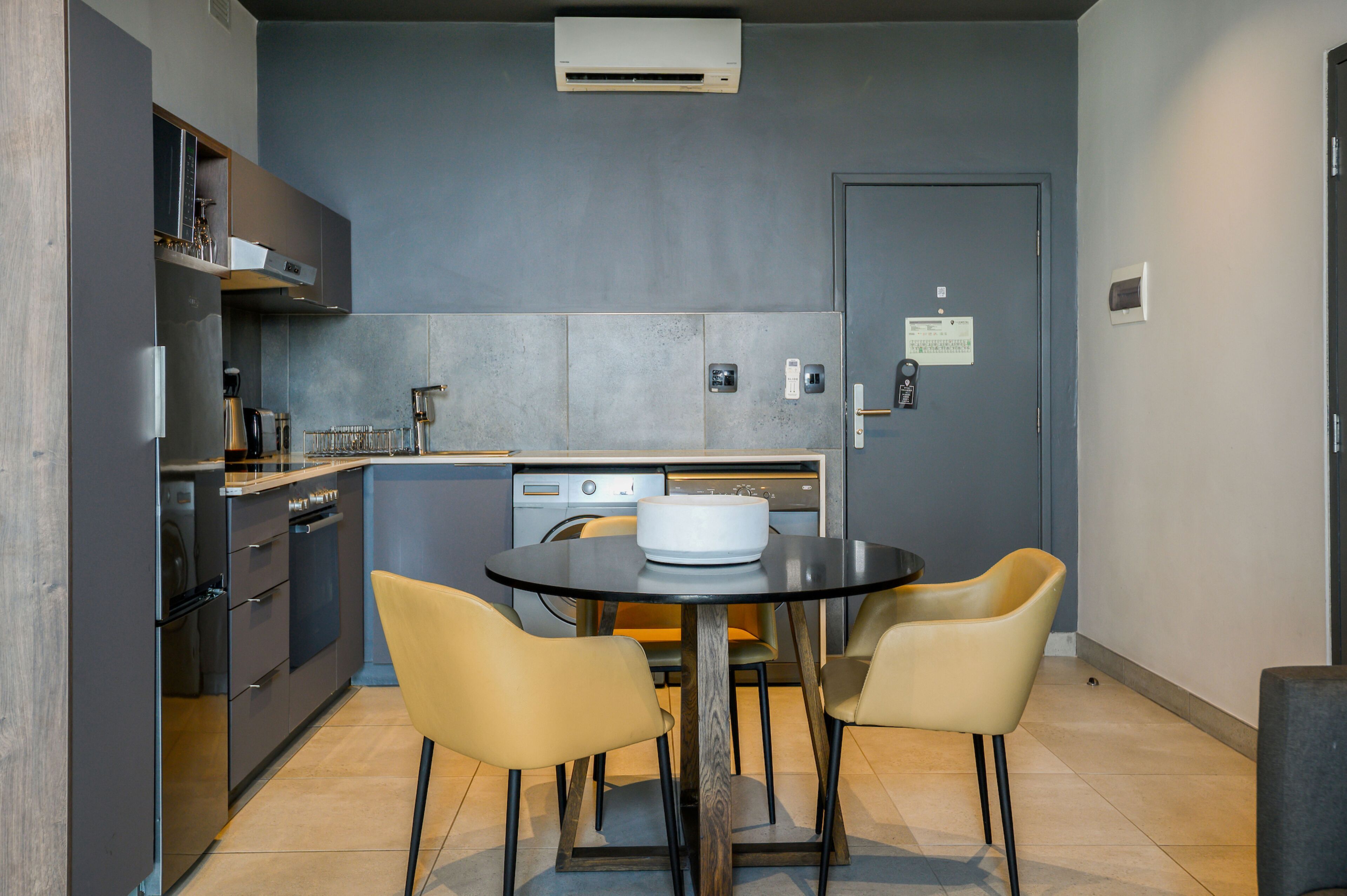 A compact kitchen with modern appliances, a dining table with chairs, and a door with a notice.