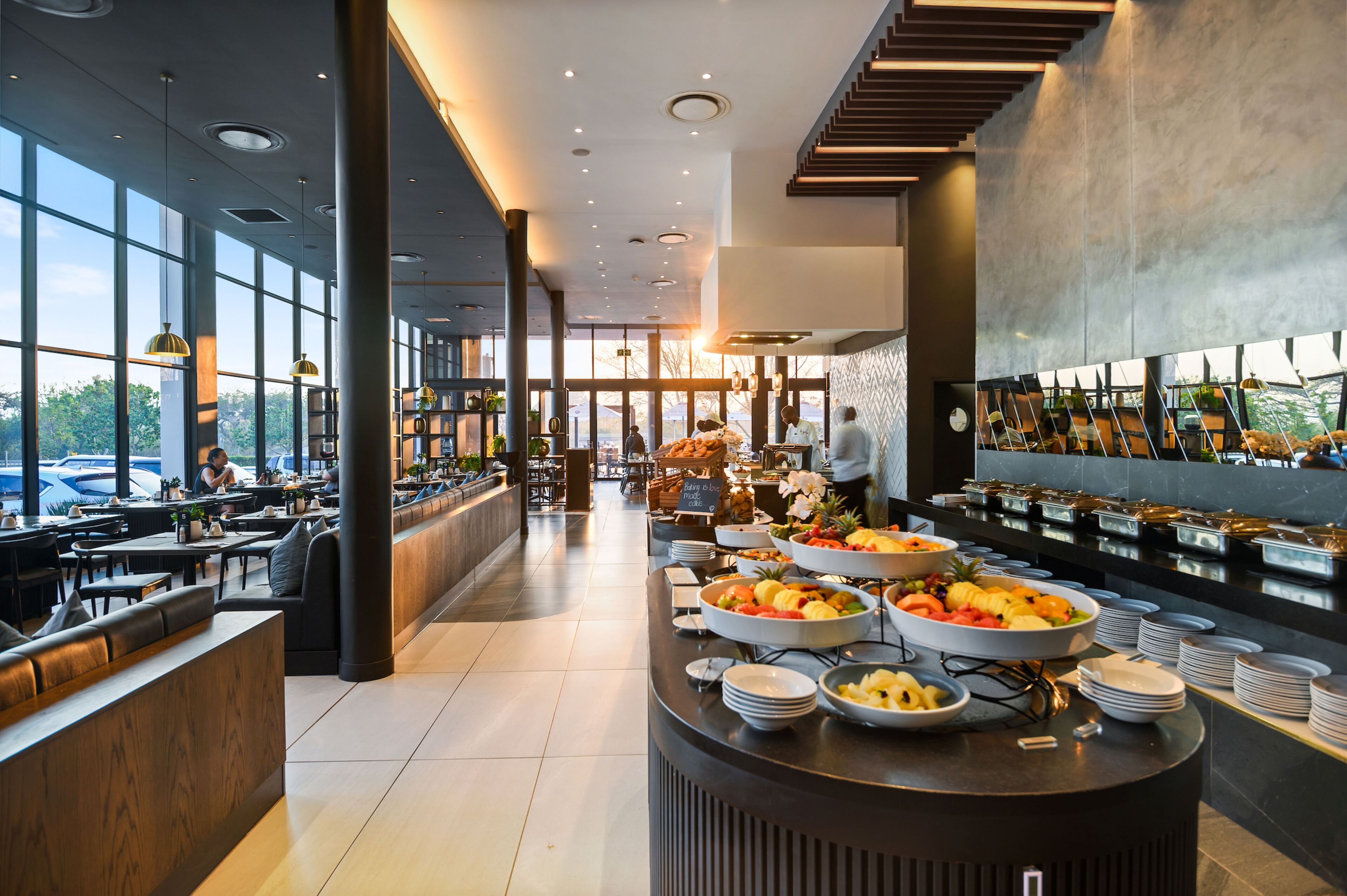 A modern hotel lobby with a buffet area, seating arrangements, and large windows offering a view of the outdoors.