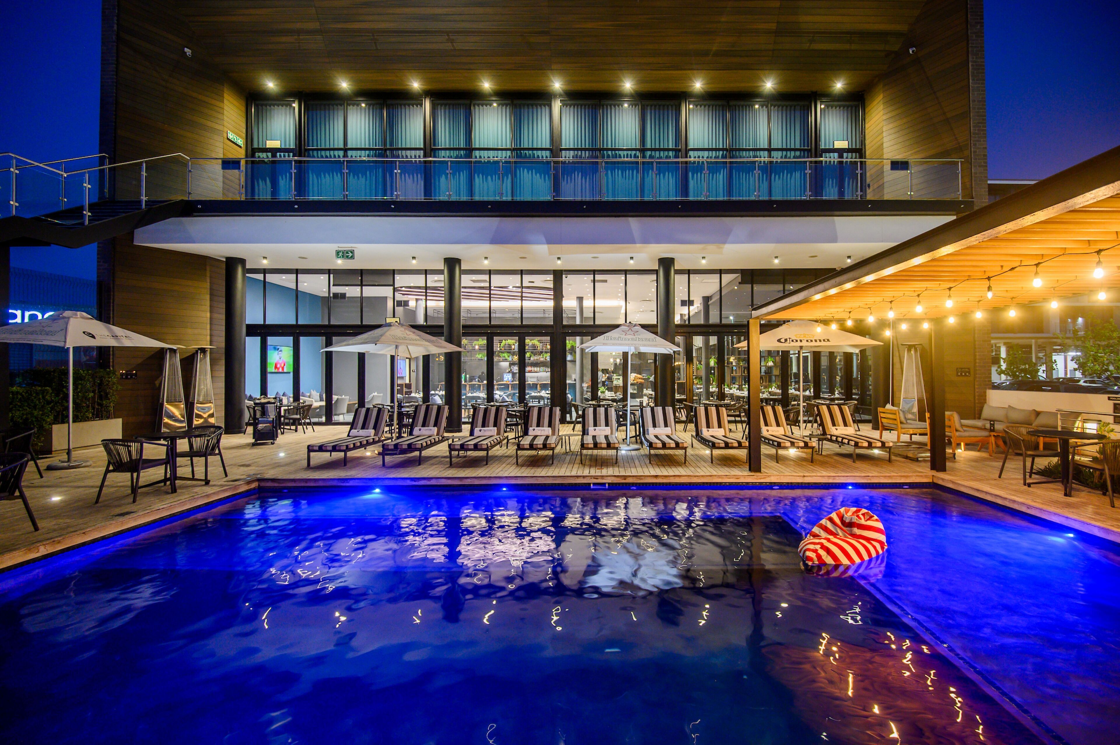 A modern hotel with a rooftop pool area, outdoor seating, and a dining area.