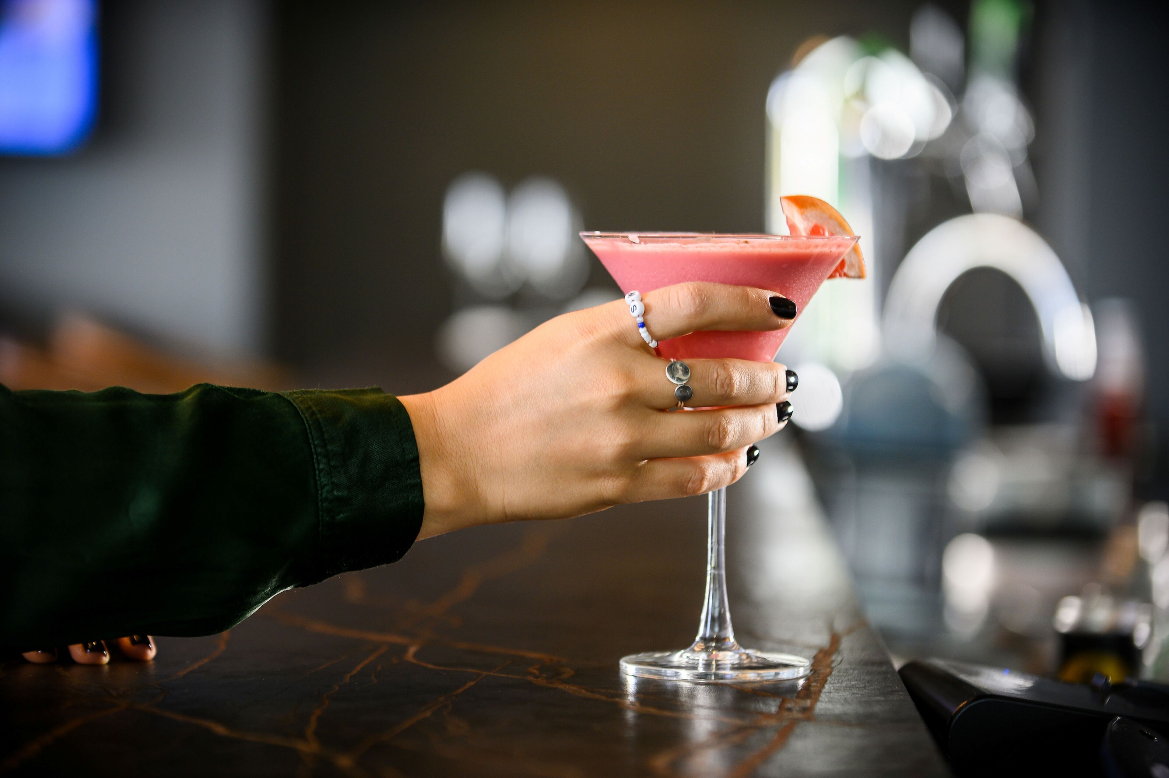 A hand holding a pink cocktail with an orange garnish.