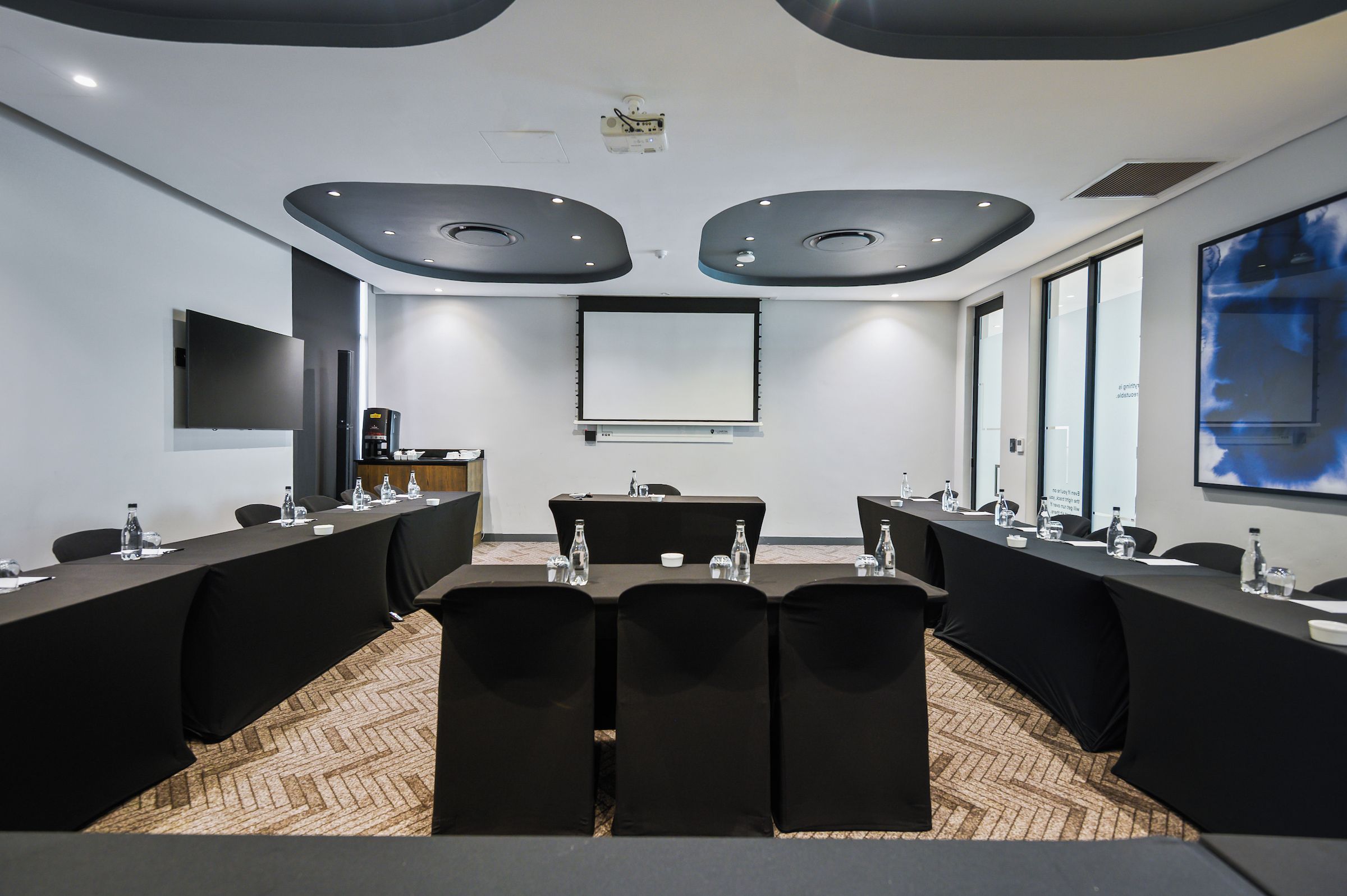 Un salón de conferencias con una larga mesa, sillas, una pantalla de proyector y un amplio ventanal.