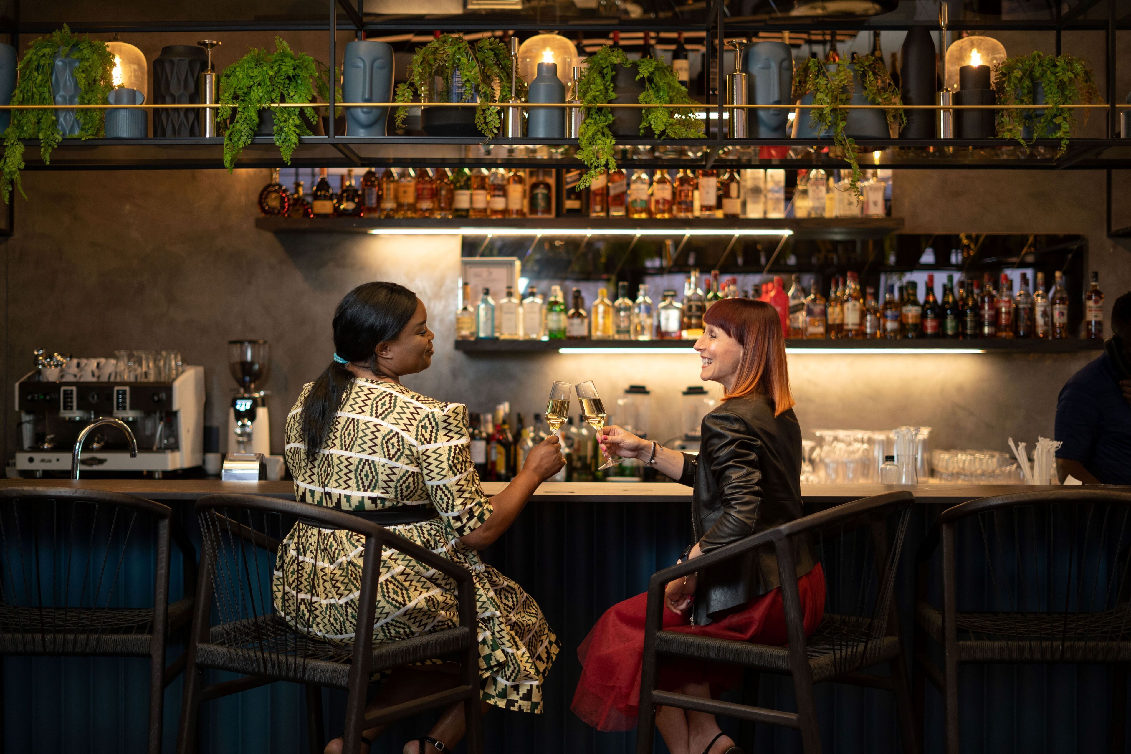 Eine Bar mit Korbstühlen, Flaschenregalen und hängenden Pflanzen.