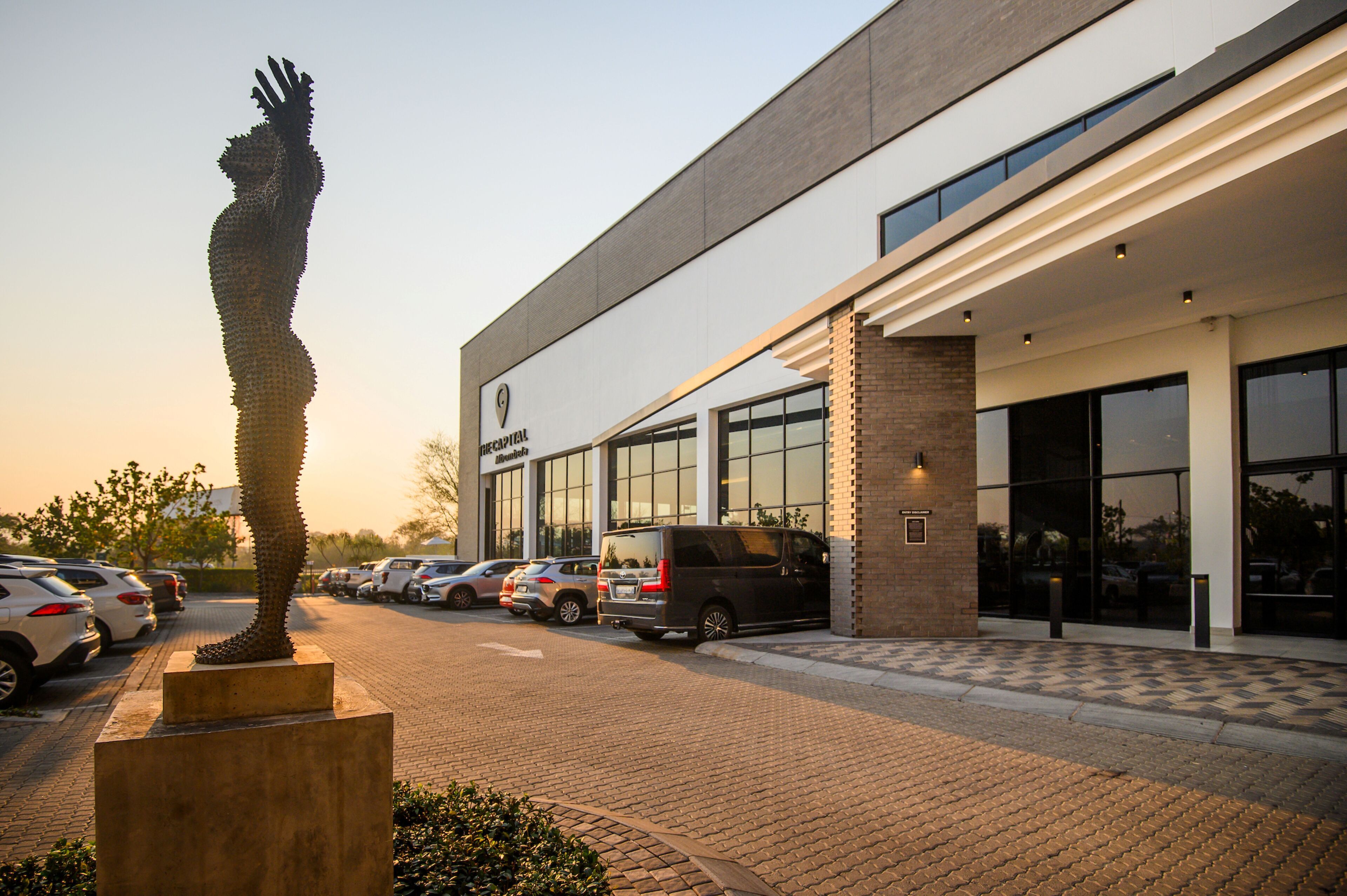 Un bâtiment moderne doté d’un parking, d’une sculpture et d’une enseigne indiquant « The Capital Hotel ».