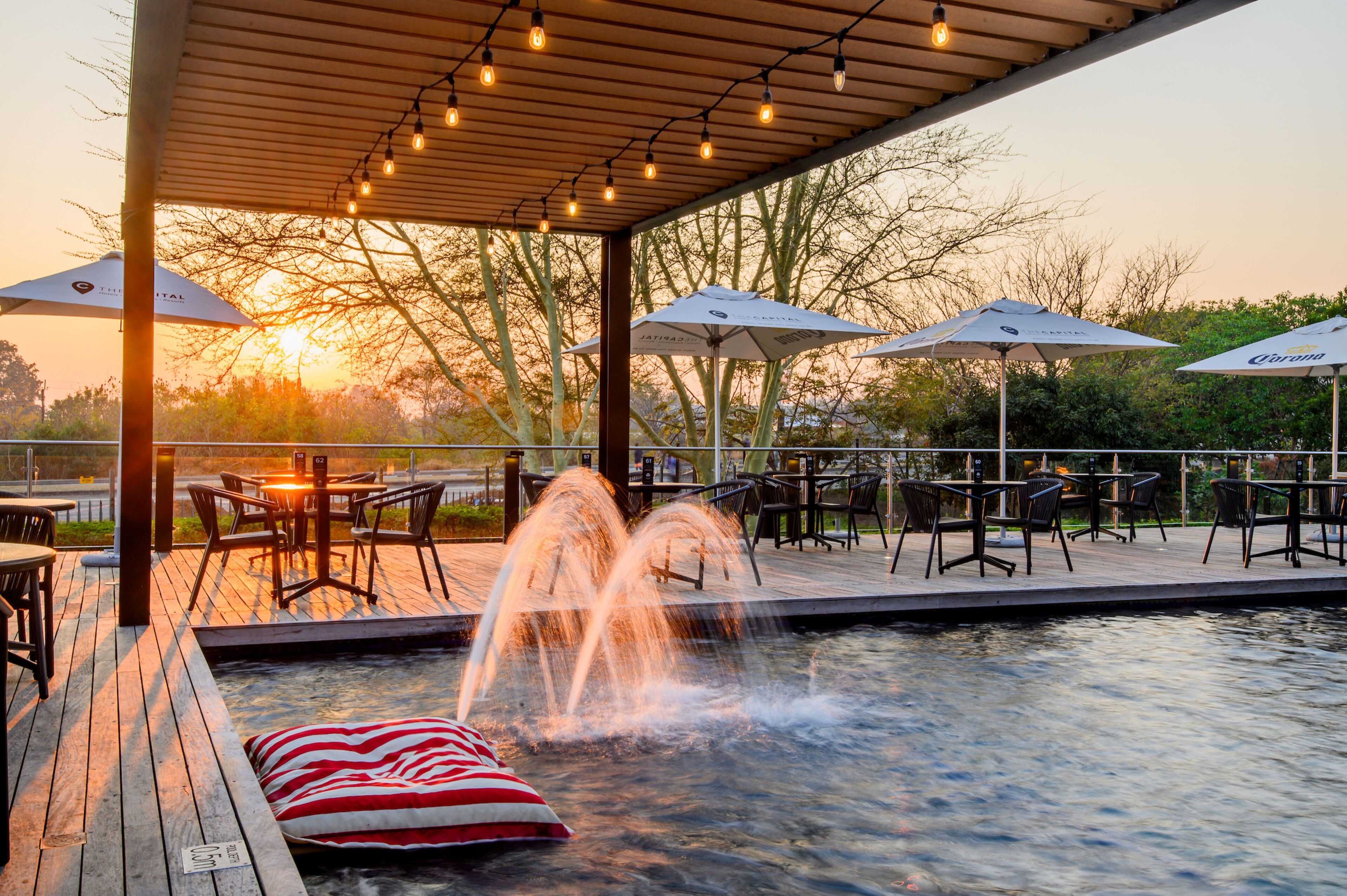 Un patio al aire libre con mesas y sillas, una piscina con fuente de agua y sombrillas.
