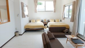 Ein Hotelzimmer mit zwei Betten, einem Sofa, einem kleinen Tisch und einem Fenster mit Vorhängen.