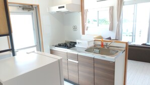 Eine kleine Küche mit Gaskochfeld, Spüle und einem Fenster mit Vorhängen.