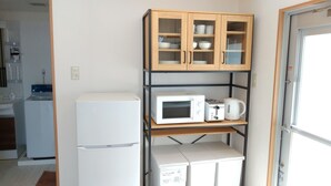Eine kompakte Küche mit einem weißen Kühlschrank, einer Mikrowelle, einem Toaster und einem Wasserkocher auf einer Ablagefläche.