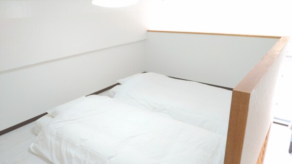 Una habitación pequeña con cama individual, ropa de cama blanca y cabecera de madera.