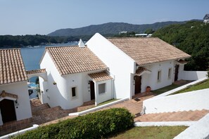 Un edificio blanco con techo de tejas, piscina y vistas a un lago y montañas.