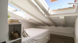 A small, compact room with a skylight, a bed, a shelf with books, and a decorative item. - ROYAL OPERA MADRID (Madrid)