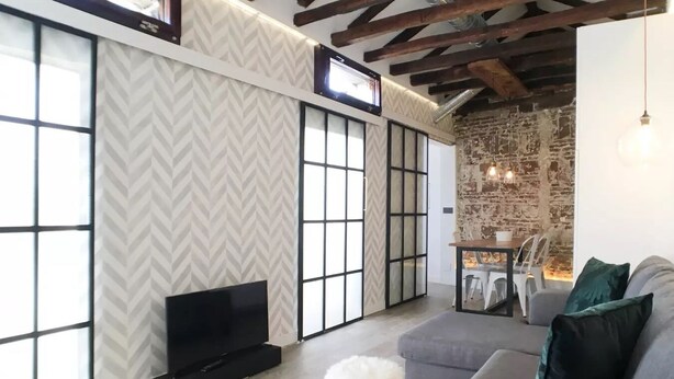 A modern living room with a large TV, a grey sofa, and a stone wall. - ROYAL OPERA MADRID (Madrid)
