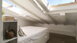 Een kleine, compacte kamer met dakraam, een bed, een plank met boeken en een decoratief object.