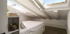 A small, compact room with a skylight, a bed, a shelf with books, and a decorative item. - ROYAL OPERA MADRID (Madrid)