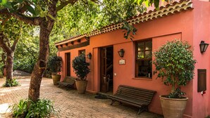 Un bâtiment rose avec un toit en tuiles, des plantes en pot et des bancs.