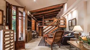 Un intérieur rustique avec des poutres apparentes, un escalier, un coin repas et un salon comprenant un canapé et une lampe.