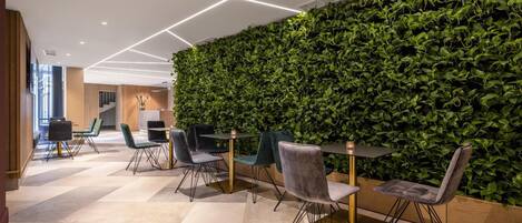 A modern indoor space with a green wall, multiple tables, and chairs arranged for dining or meetings.