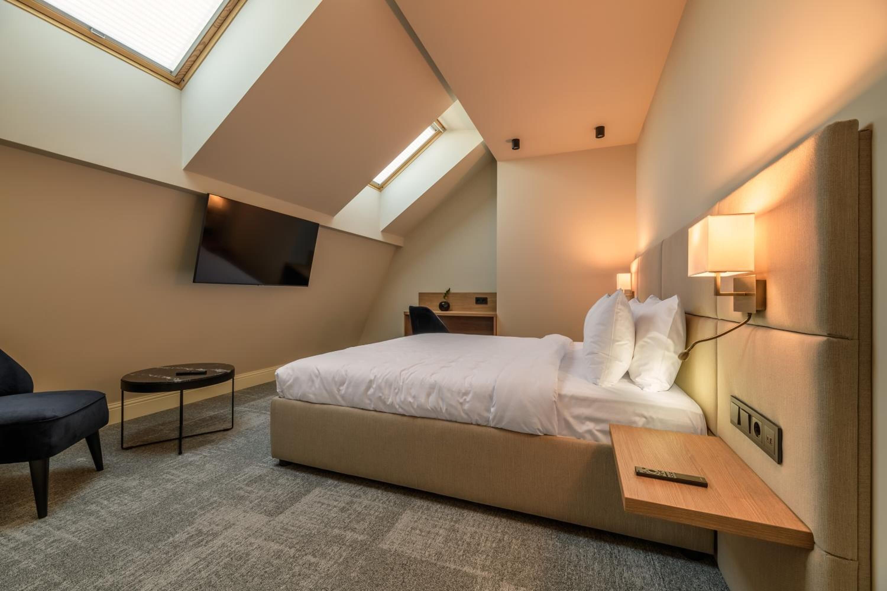Una habitación de hotel moderna con una cama grande, un televisor montado en la pared y un tragaluz.