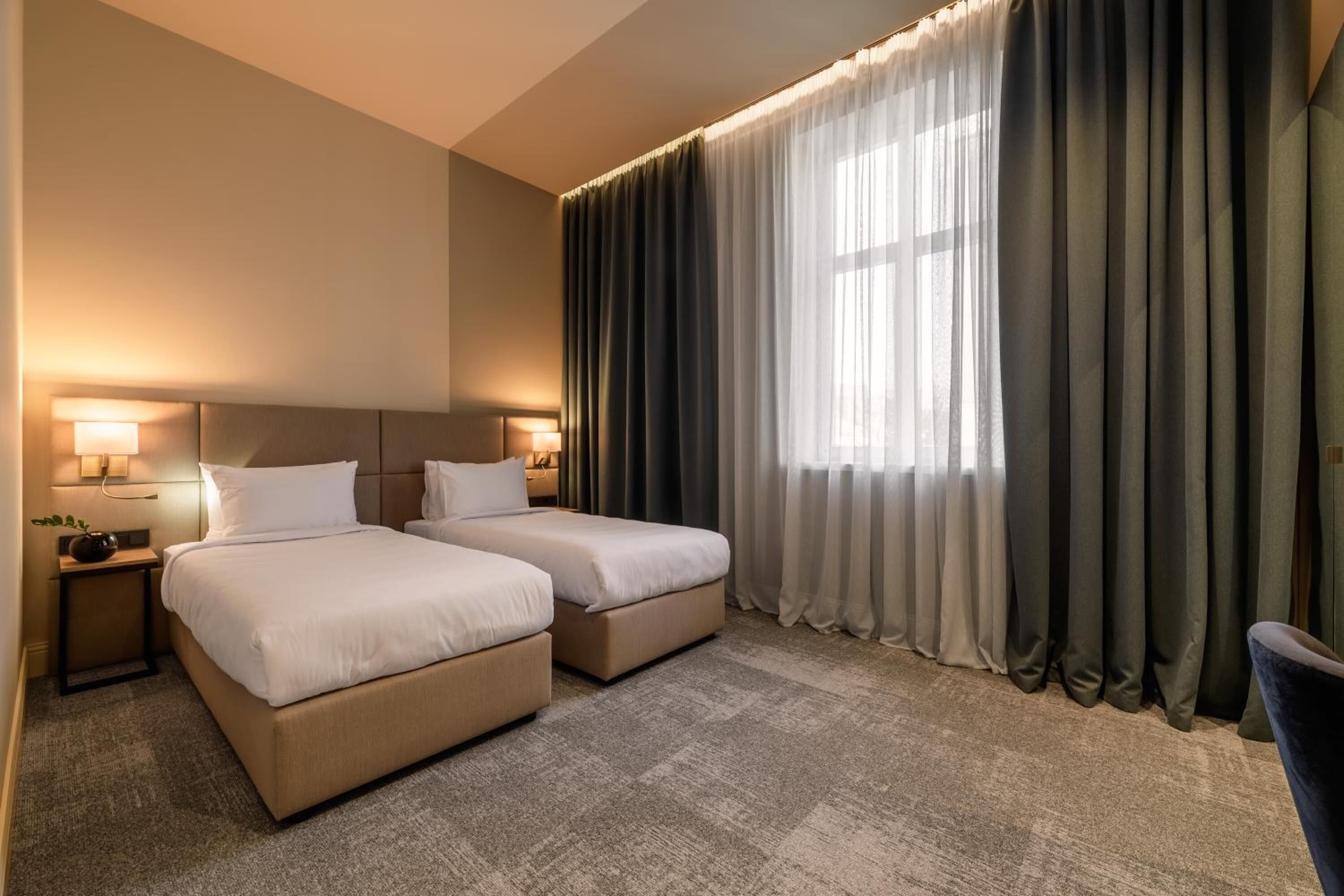 Una habitación de hotel con dos camas, un ventanal con cortinas y lámparas de noche.
