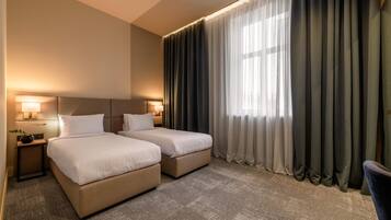 Una habitación de hotel con dos camas, un ventanal con cortinas y lámparas de noche.