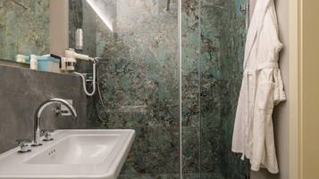 Un baño moderno con ducha de vidrio, lavamanos sobre pedestal y una bata blanca colgada en la pared.