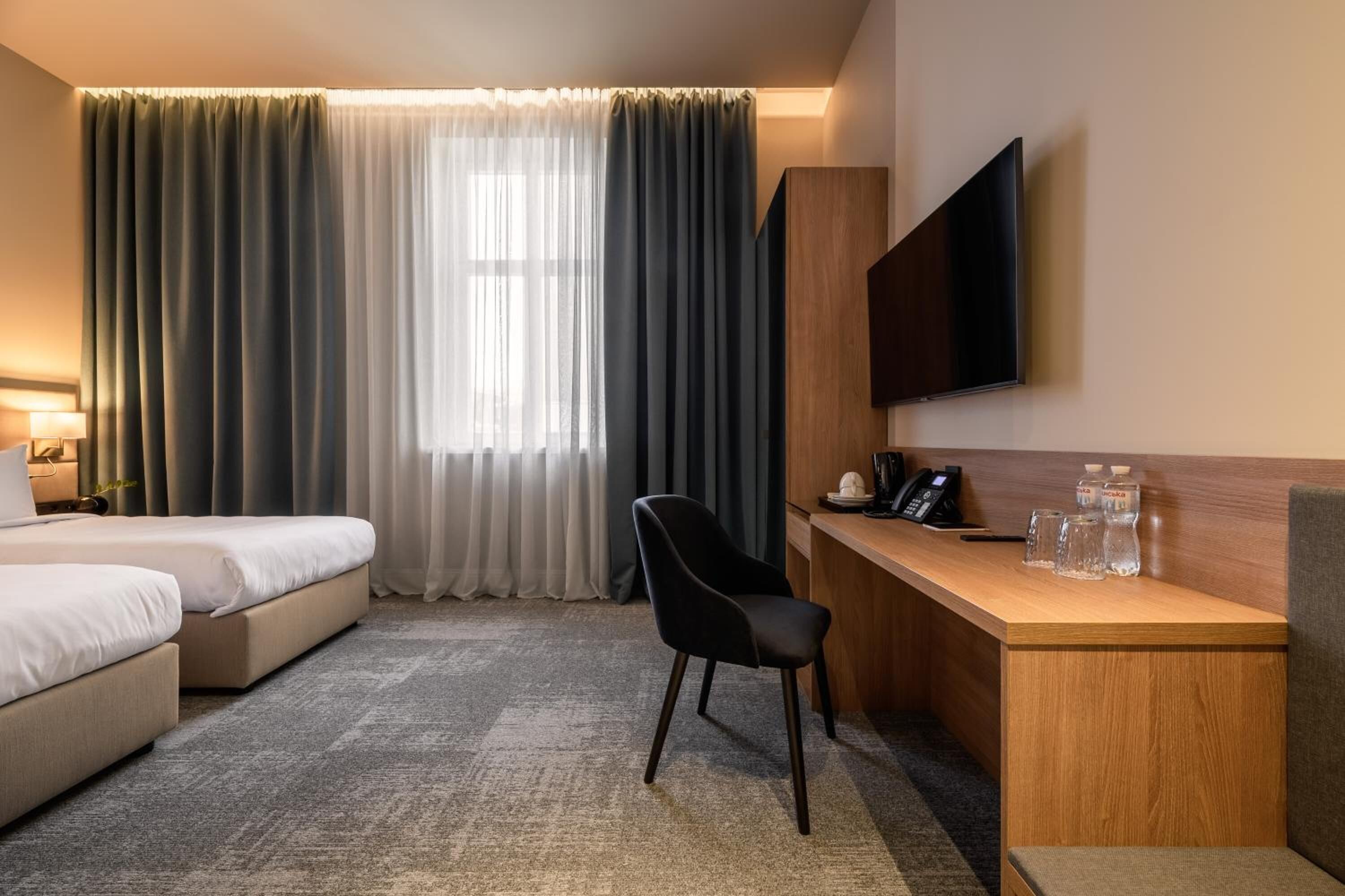 Habitación de hotel con cama, escritorio con silla, televisor y ventana con cortinas.