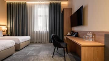Habitación de hotel con cama, escritorio con silla, televisor y ventana con cortinas.