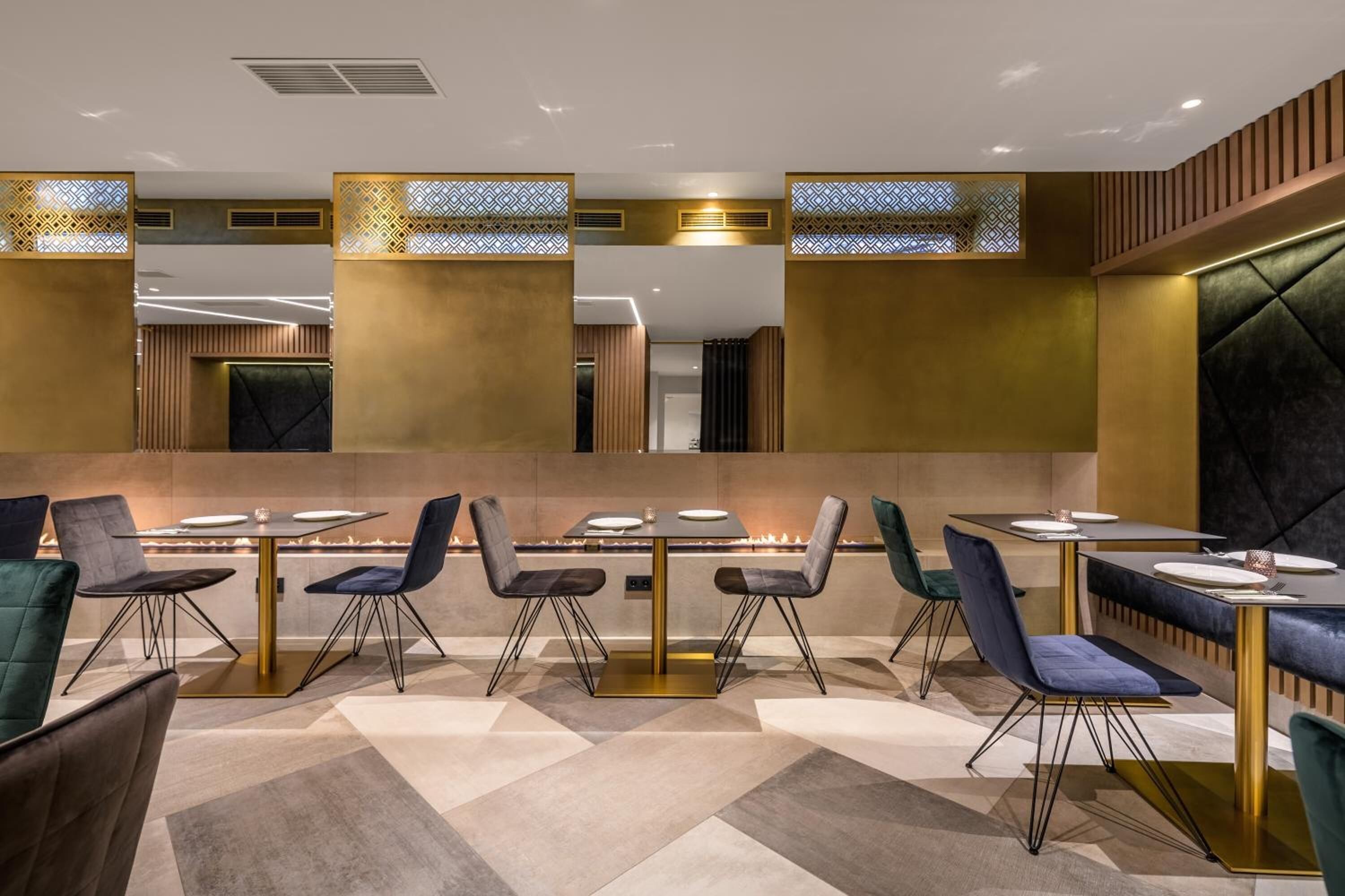A modern restaurant with multiple tables and chairs, a central fire feature, and decorative panels.